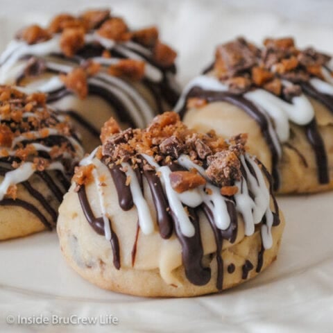 A white plate with toffee cookies drizzled with chocolate and toffee bits.