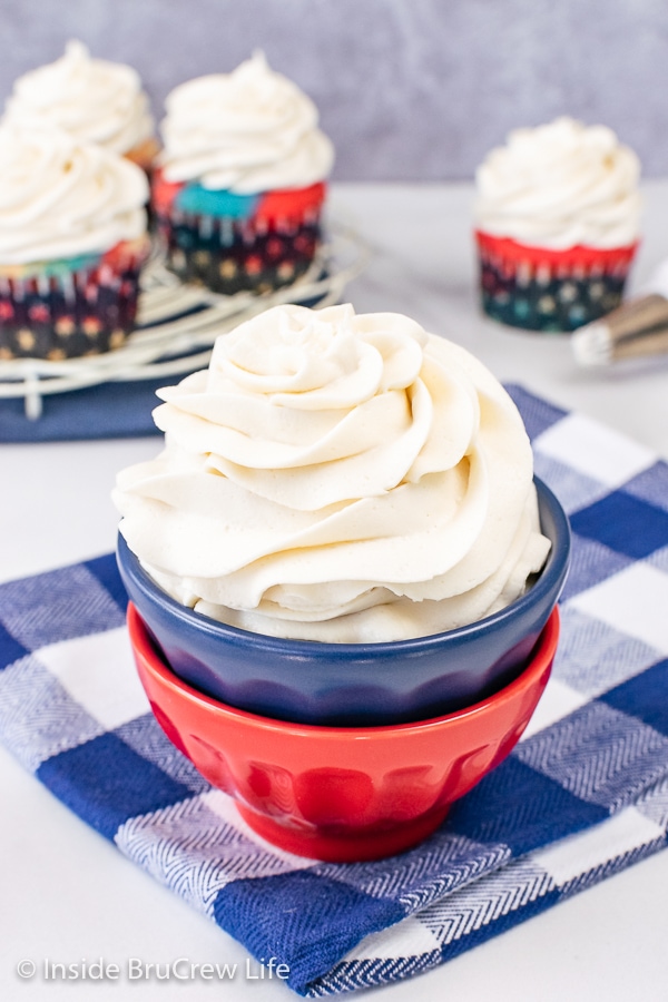 A stack of red and blue bowls filled with a big swirl of vanilla frosting in it.