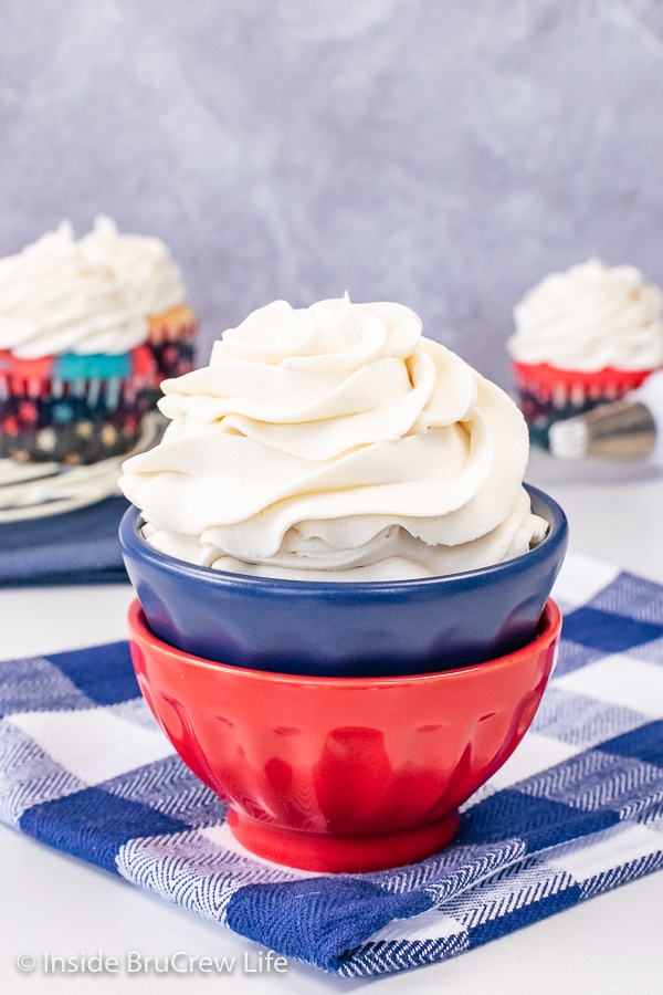 Two red and blue bowls stacked together with a swirl of vanilla buttercream frosting in it.