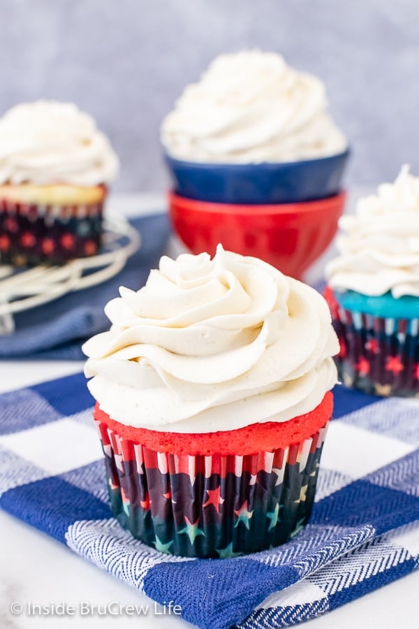 A red cupcake on a blue towel topped with a big swirl of vanilla frosting.