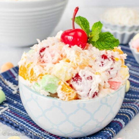 A white bowl filled with ambrosia salad and topped with cherries and mint leaves.