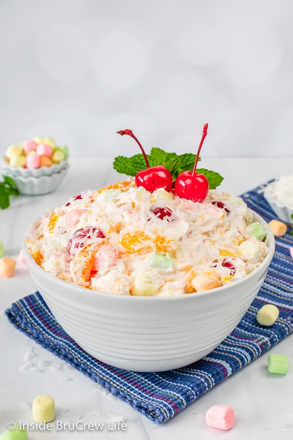 A white bowl filled with Ambrosia dessert and topped with cherries and mint leaves.