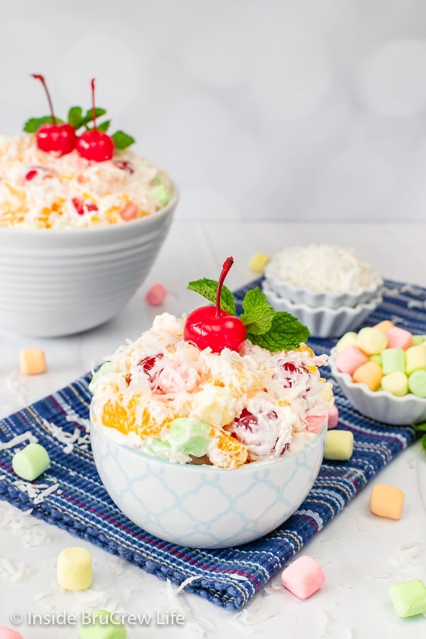 Two white bowls on a blue towel filled with an easy ambrosia salad.
