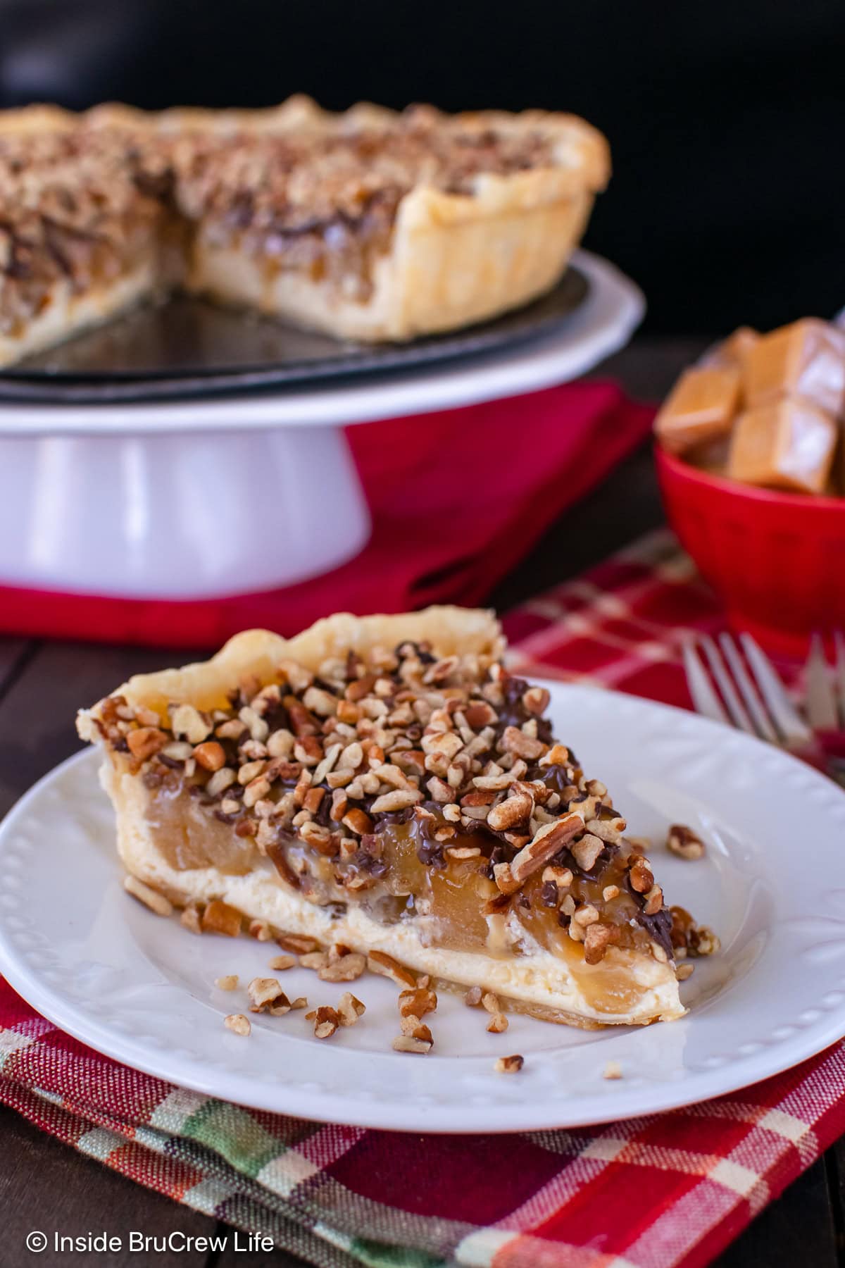 A slice of apple cheesecake tart with caramel and pecans.