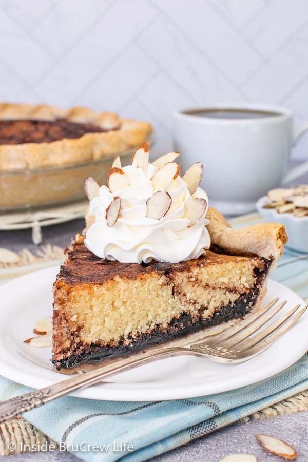 A white plate with a slice of chocolate Funny Cake topped with whipped cream and almonds.