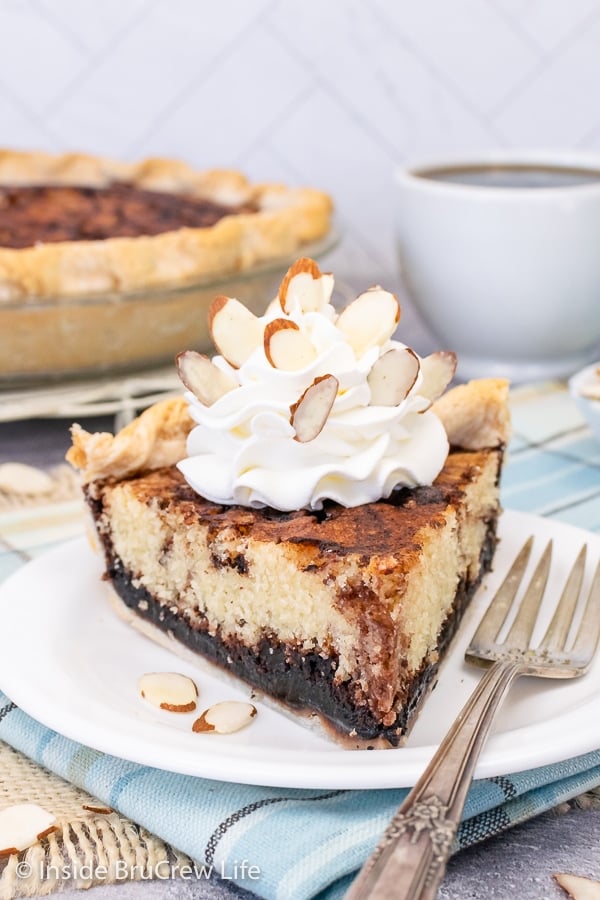 A white plate with a slice of chocolate funny cake topped with whipped cream and almonds.