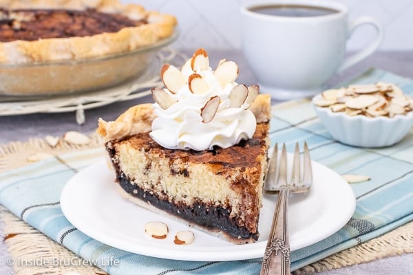 A white plate with a slice of chocolate funny cake topped with Cool Whip and almonds.