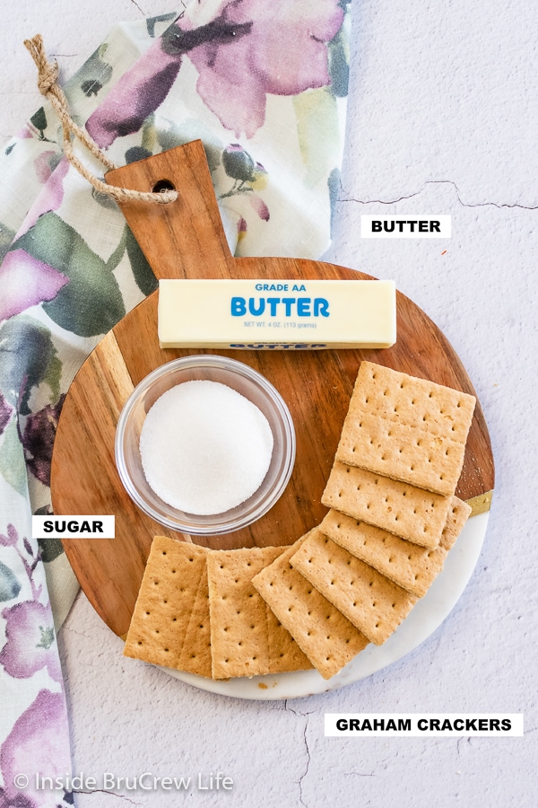 Overhead picture of a round wooden board with ingredients needed to make a graham cracker crust.