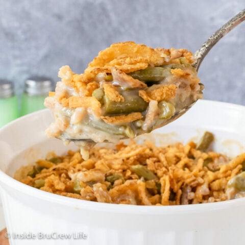 A white casserole dish filled with green bean casserole and a spoon lifting some out.