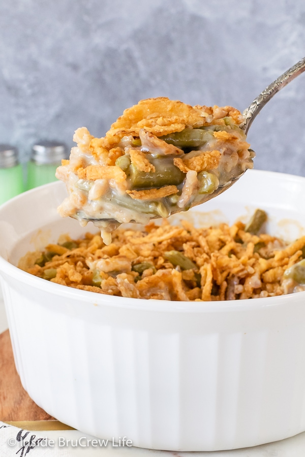 A white casserole dish filled with green bean casserole with a spoon lifting some out.