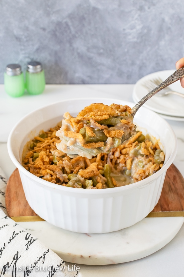 A white casserole dish filled with classic green bean casserole and a spoon lifting some out.