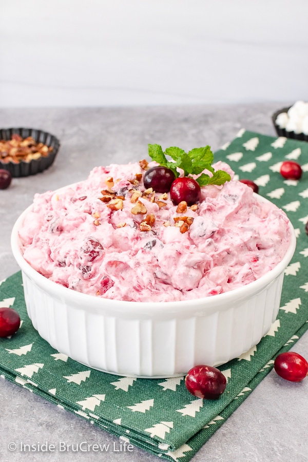 A large white serving bowl on a green towel filled with a creamy cranberry fluff dessert.