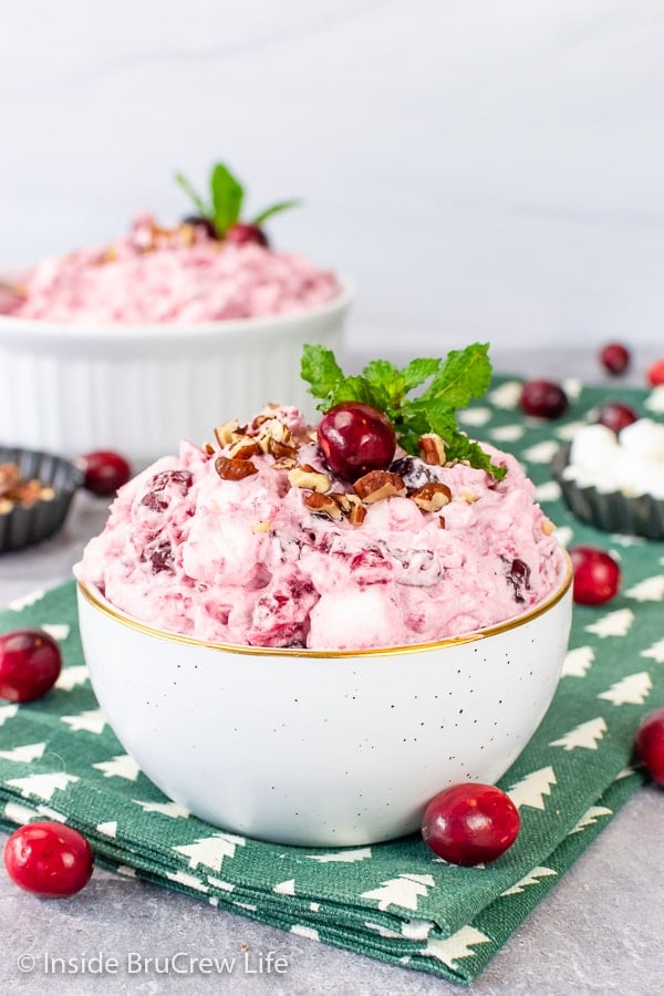 A white bowl on a green towel filled with pink cranberry fluff salad and topped with pecans and fresh cranberries.