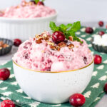 A white bowl on a green towel filled with pink fluffy cranberry fluff salad.