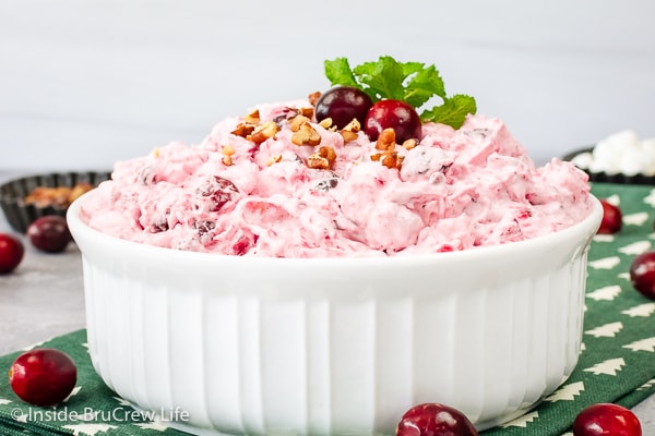 A large white serving bowl filled with pink cranberry fluff and topped with pecans and fresh cranberries.