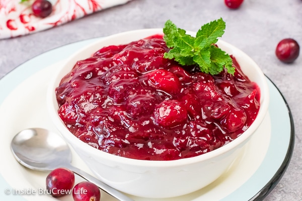 A white bowl on a plate filled with homemade cranberry sauce and garnished with mint leaves.