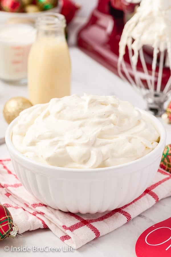 A white bowl on a holiday towel filled with fluffy mounds of homemade whipped cream made with eggnog.