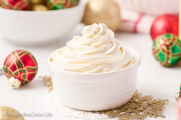 A swirl of homemade eggnog whipped cream in a white bowl with red and gold ornaments around the bowl.