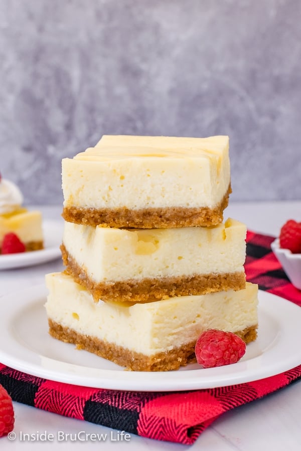 A white plate with three lemon cheesecake bars stacked on top of each other on it.