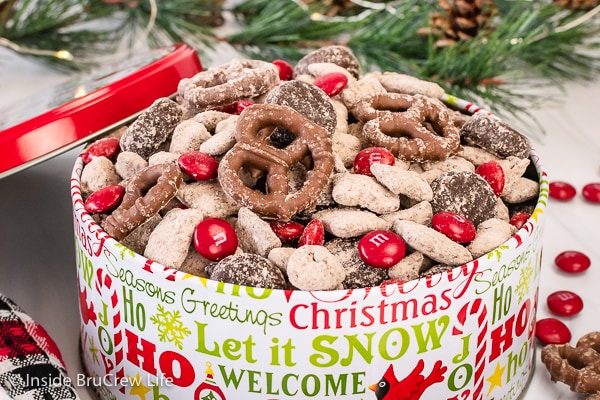 A metal tin filled with reindeer snack mix made with chocolate covered pretzels and candies.