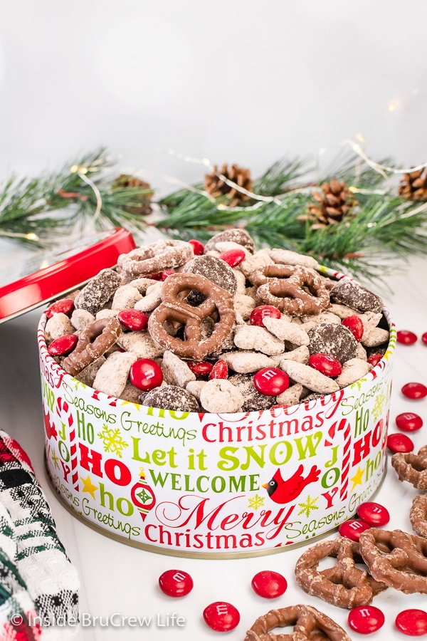 A Christmas tin filled with brownie reindeer chow with chocolate covered pretzels and candies.