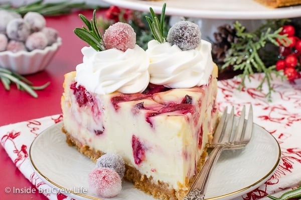 A white plate with a slice of white chocolate cheesecake with swirls of cranberry sauce in it.
