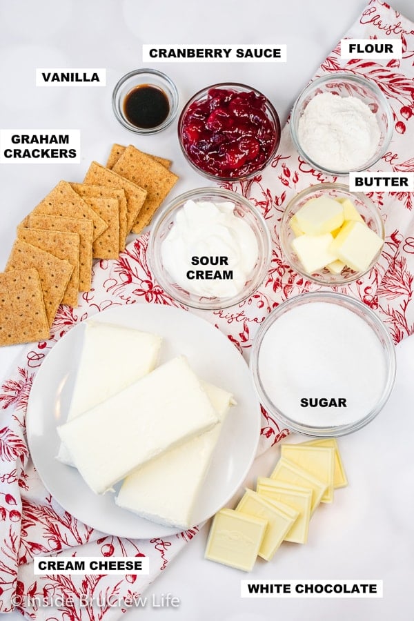 Overhead picture of a white board with bowls of ingredients needed to make a cranberry cheesecake.