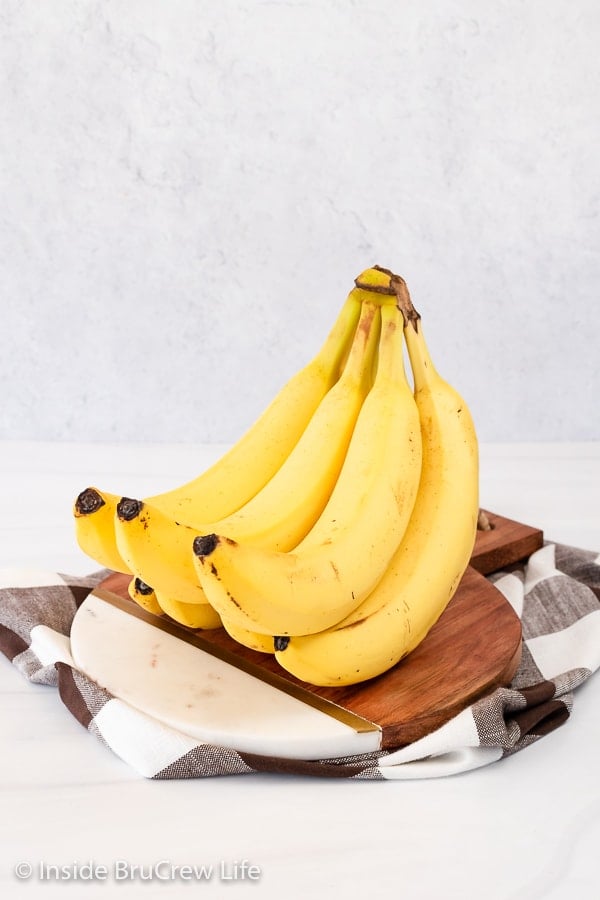 A bunch of yellow bananas on a cutting board on a white board.