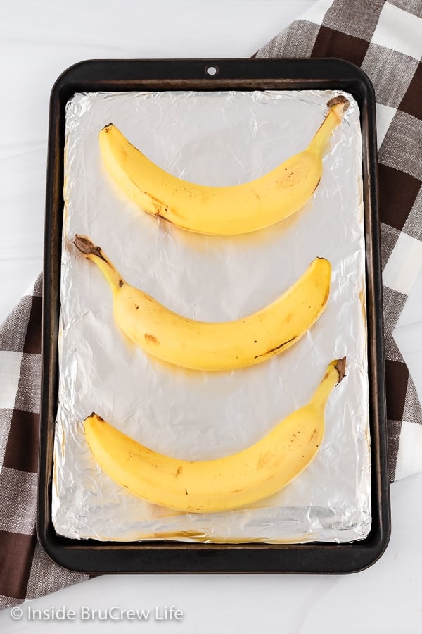 A brown sheet pan with three yellow bananas lying on it.