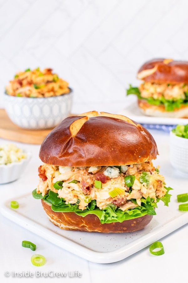 A white plate with a pretzel bun filled with chicken salad on it.