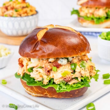 A white plate with a pretzel bun filled with chicken salad.