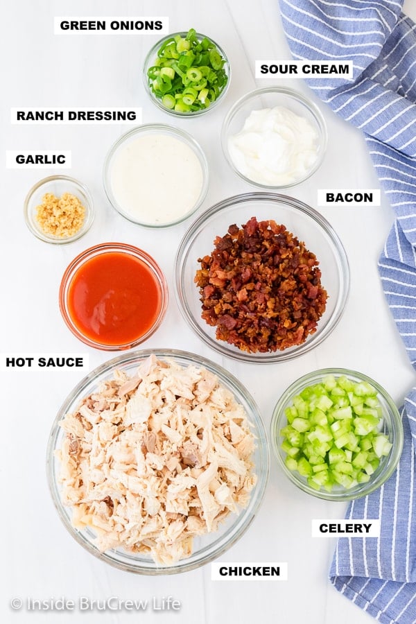 A white board with bowls of ingredients needed to make a spicy chicken salad recipe.