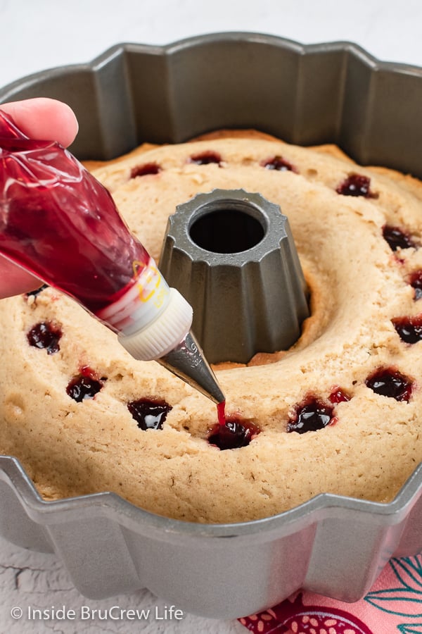 A bundt cake with holes being filled with raspberry jam.