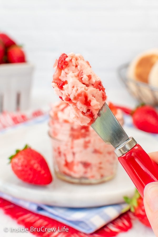 A knife with strawberry butter on it held up in the air.