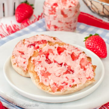 A white plate with an english muffin spread with pink strawberry butter on it.