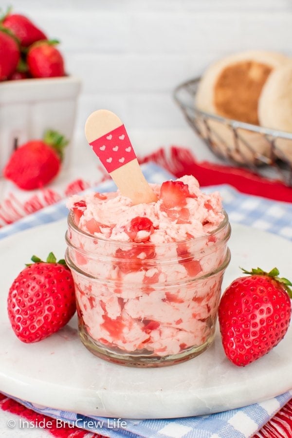 A clear jar filled with pink butter loaded with strawberry chunks.