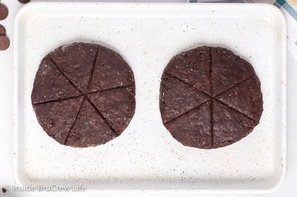 A white tray with chocolate scone dough circles on it.