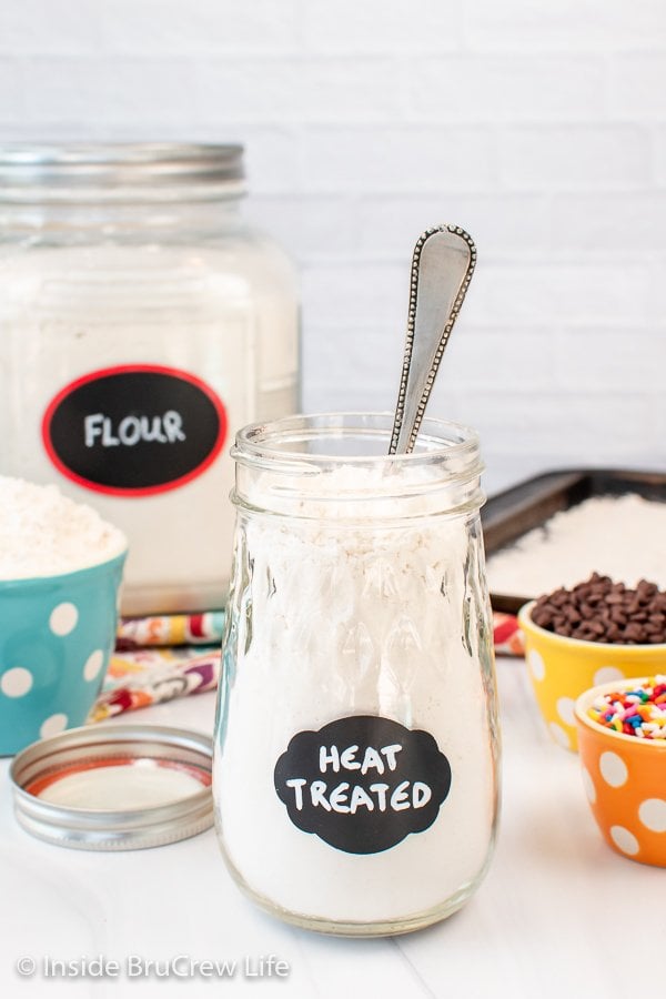 A clear jar of heat treated flour with a spoon in it.