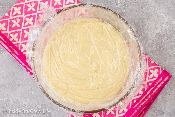 A clear bowl of pudding with plastic wrap on top.