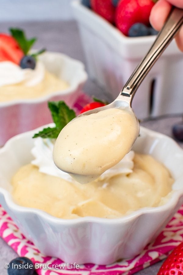 A spoon with vanilla pudding on it being held up.