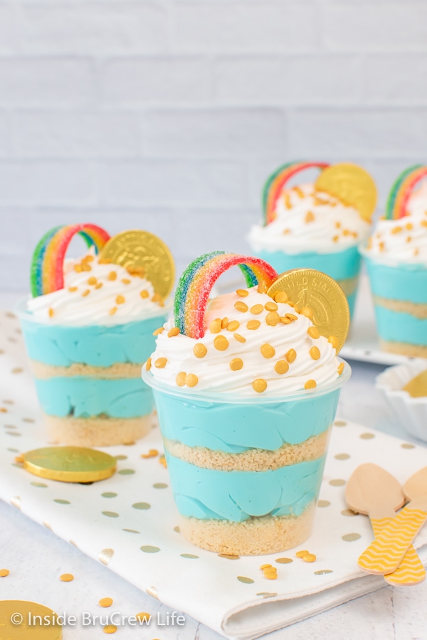 Two blue cheesecake cups topped with cool whip and rainbow candy.