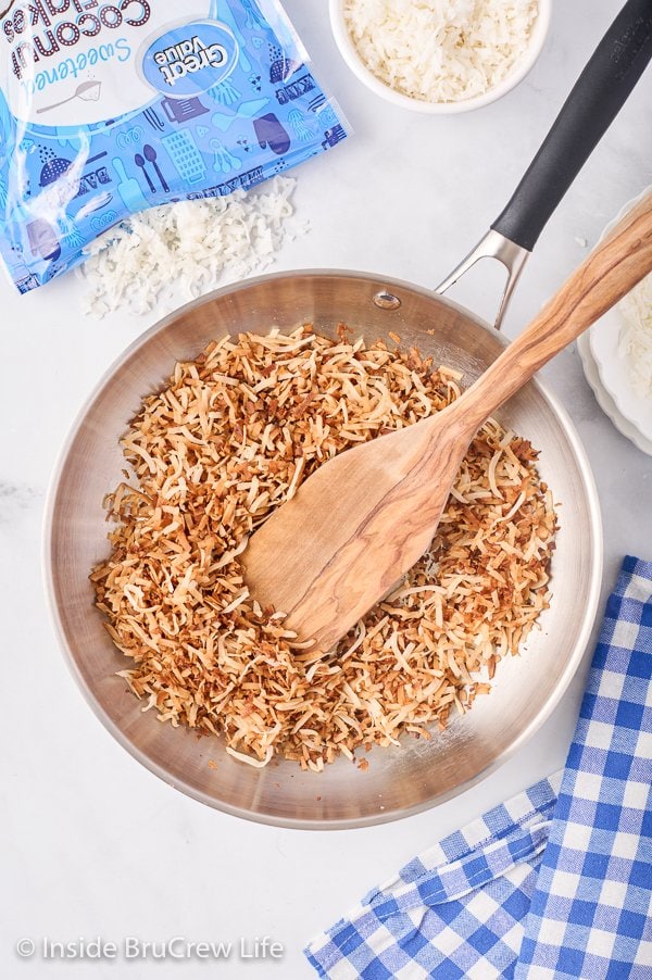 A skillet pan filled with toasted coconut and a wooden spoon.