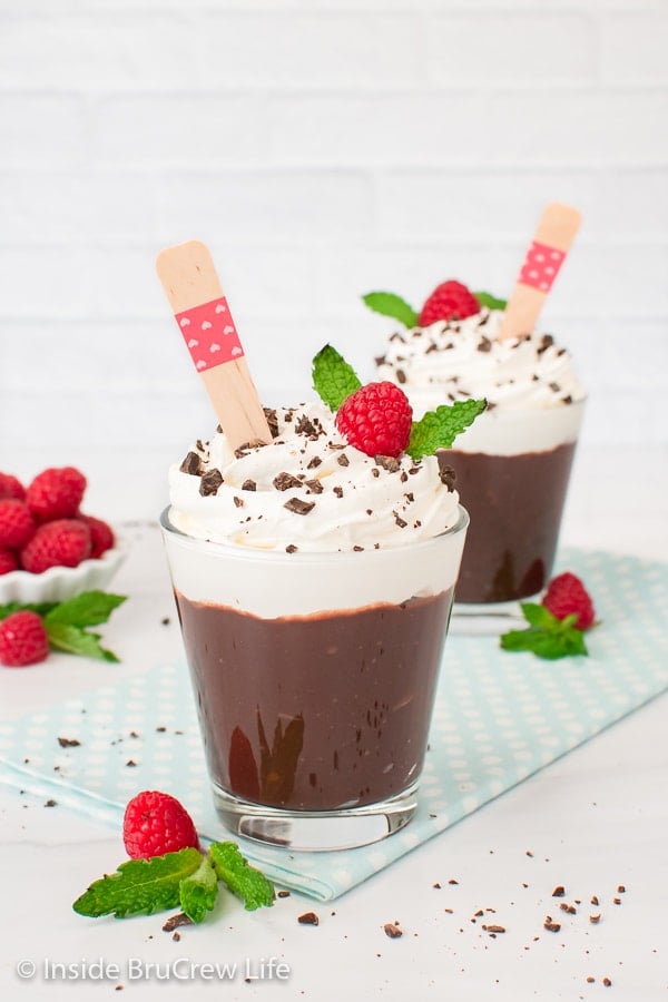 Two cups of dark chocolate pudding with spoons in them.