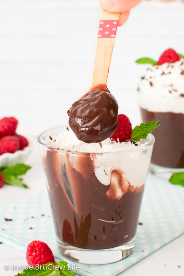 A cup of chocolate pudding topped with whipped cream with a spoon of pudding above it.