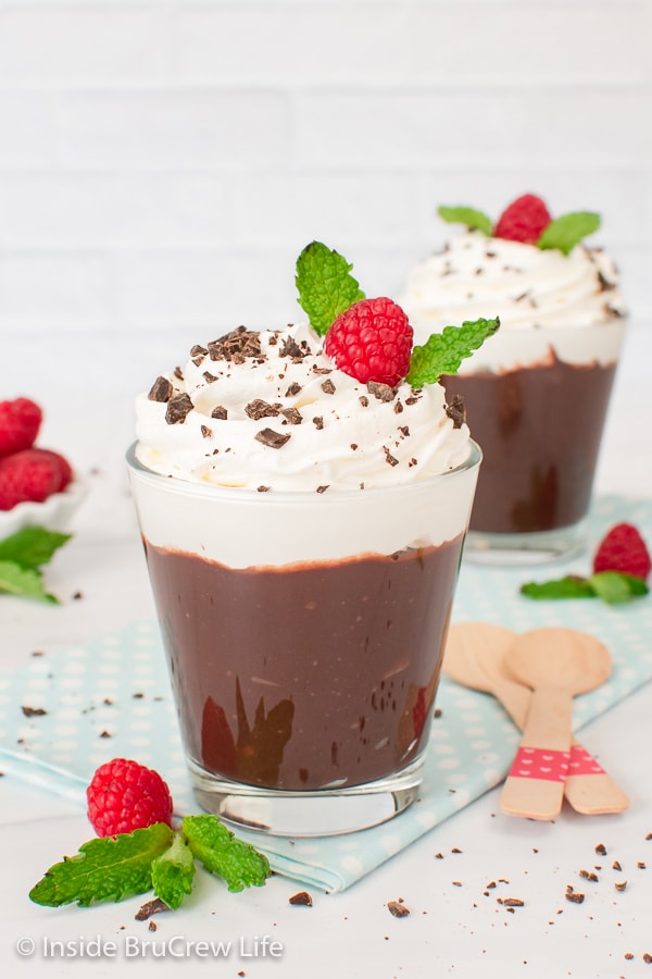 Two chocolate pudding cups topped with whipped cream and berries.