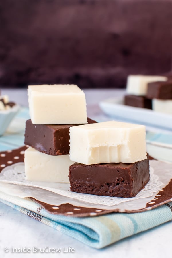 Chocolate and vanilla fudge squares stacked together on a paper.