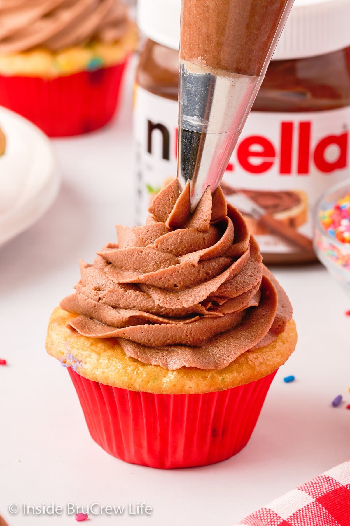 A cupcake being topped with a swirl of chocolate frosting.