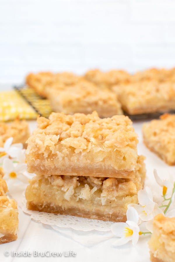 Two pineapple crumble bars stacked together on a white board.