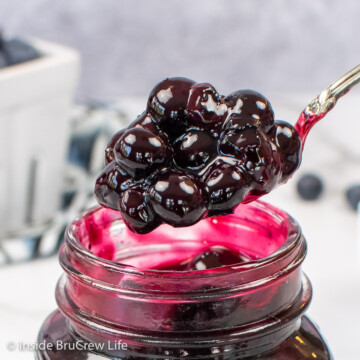 A clear jar of blueberry pie filling with a spoon lifting some out.