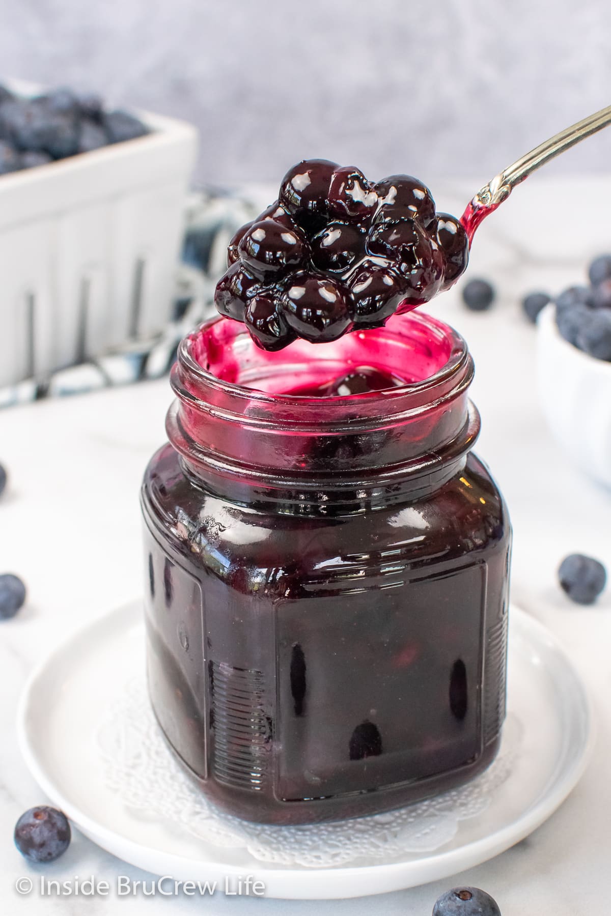A clear jar of blueberry pie filling with a spoon lifting some out.